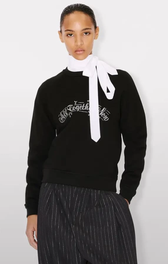 Dziewczyna w czarnej bluzie, eleganckich spodniach i z białą kokardą pod szyją