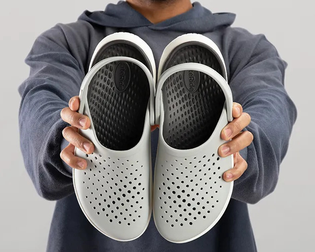 Mężczyzna trzymający w dłoniach szare buty Crocs