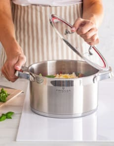 Ręce gospodyni z fartuchu na pokrywce i garnku