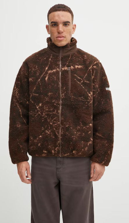 Chłopak w brązowych spodniach i brązowej bluzie z pomarańczowymi akcentami