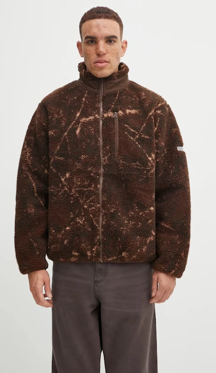 Chłopak w brązowych spodniach i brązowej bluzie z pomarańczowymi akcentami