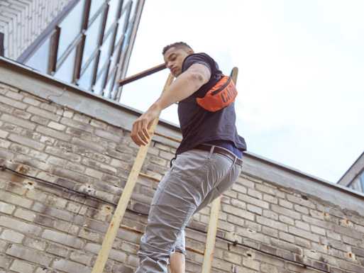 Mężczyzna wchodzący po drabinie na mur z pomarańczową nerką na pleacach