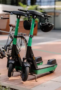 Dwie zielone hulajnogi elektryczne zaparkowane na chodniku