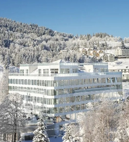 Biały budynek hotelowy pośród pokrytego śniegiem lasu i gór