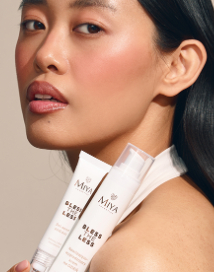 Azjatka patrząca w obiektyw z kosmetykami w białych opakowaniach w ręce