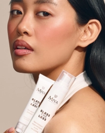 Azjatka patrząca w obiektyw z kosmetykami w białych opakowaniach w ręce