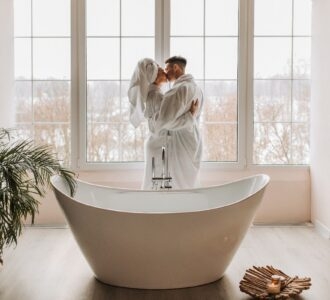 Para w szlafrokach całująca się na tle okien w łazience z wanną